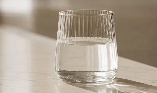 Un pahar cu nervuri de Kangen Water® limpede pe un blat însorit